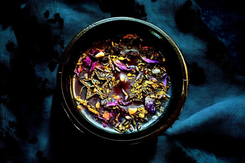 May include: A black bowl filled with a purple candle with gold glitter, dried flowers, and a gold star charm.