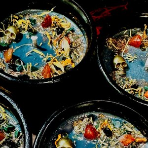 Puede incluir: Tres portavelas negros en forma de caldero con cera azul, detalles de calavera dorada y hierbas y flores secas.