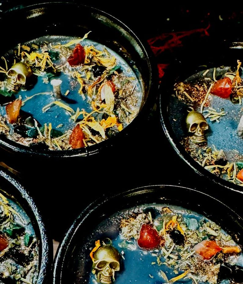 Puede incluir: Tres portavelas negros en forma de caldero con cera azul, detalles de calavera dorada y hierbas y flores secas.