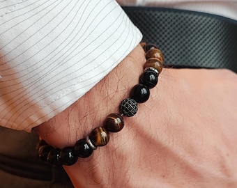 Puede incluir: Un brazalete de cuentas con ojo de tigre marrón, ónix negro y cuentas plateadas.
