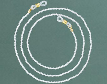 May include: A white beaded eyeglass chain with gold-toned clasps. The chain is made of small, round beads and is designed to hold eyeglasses securely around the neck.