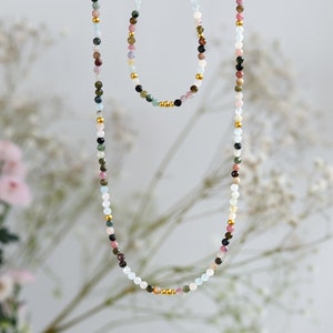 May include: A long and short necklace set with colorful gemstone beads and gold accents. The necklace is made of aquamarine, pink tourmaline, green tourmaline, black tourmaline, and other gemstones.