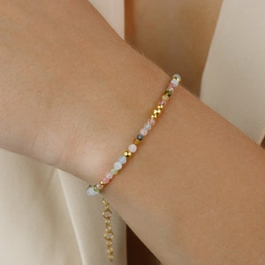 May include: A delicate bracelet featuring a mix of pastel-colored gemstone beads and gold accents. The bracelet has a simple chain closure.