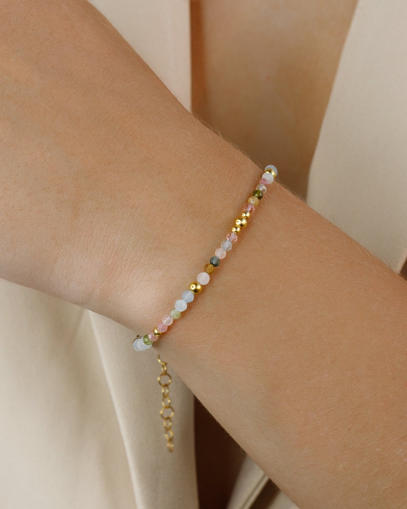 May include: A delicate bracelet featuring a mix of pastel-colored gemstone beads and gold accents. The bracelet has a simple chain closure.