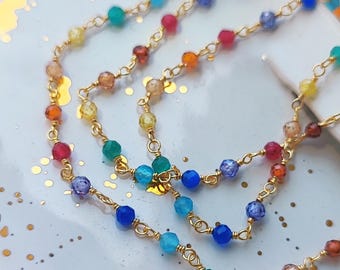 May include: A gold chain necklace with rainbow colored beads. The beads are faceted and have a variety of shapes.