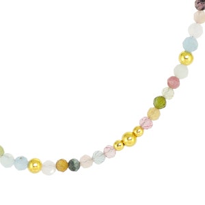 May include: A multi-colored gemstone beaded necklace with gold accents. The necklace features a variety of round, faceted gemstones in shades of pink, green, blue, and yellow.
