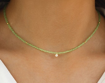 May include: A delicate gold necklace with a small, clear gemstone pendant. The necklace is made of tiny green beads and gold beads.