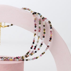 May include: Multi-strand necklace with small, colorful gemstone beads. The necklace is made of pink, blue, green, and black beads.