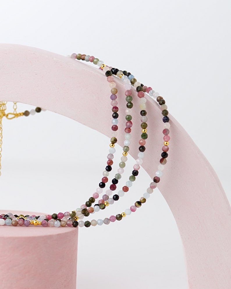May include: Multi-strand necklace with small, colorful gemstone beads. The necklace is made of pink, blue, green, and black beads.