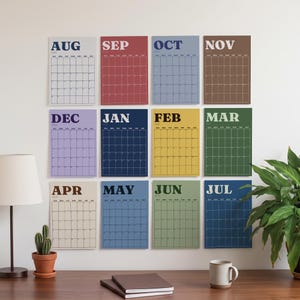 May include: A wall calendar set featuring twelve individual rectangular sheets, each representing a month from August to July. Each sheet displays the month name in bold capital letters and a grid for dates in various colors including red, blue, yellow, green, brown, and purple.
