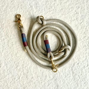 May include: A beige rope dog lead with a red and blue striped accent and gold hardware.