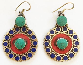 May include: A pair of ornate earrings with a circular design. Each earring features a central red circle surrounded by blue and gold accents, with a turquoise stone in the center and top. The earrings have a hook closure.