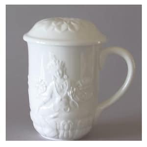 May include: White ceramic tea mug with a lid. The mug features a detailed embossed design of a seated figure, possibly a deity, and a curved handle. The lid has a floral design. The mug is designed for tea.