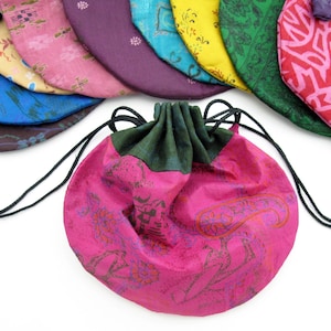 May include: A pink drawstring bag with a green lining and black drawstrings. The bag is decorated with a floral pattern and has a paisley design.