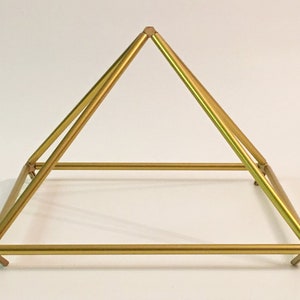 K&ouml;nnte beinhalten: Eine goldfarbene Metallpyramide mit quadratischer Basis. Die Pyramide besteht aus vier St&auml;ben, die an den Ecken miteinander verbunden sind. Die St&auml;be sind glatt und haben eine gl&auml;nzende Oberfl&auml;che.