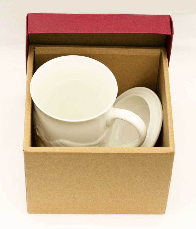 May include: A white ceramic mug with a handle and a matching saucer, packaged in a brown cardboard box with a burgundy lid.