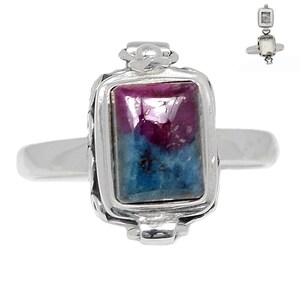 May include: A silver ring featuring a rectangular gemstone with a vibrant color combination. The gemstone showcases a mix of deep magenta and teal hues, set within a detailed silver frame. The ring's design includes decorative elements on the setting.