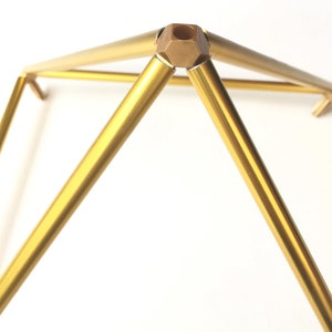 K&ouml;nnte beinhalten: Ein goldfarbener Metall-Pyramidenst&auml;nder mit einem sechseckigen Verbinder an der Spitze. Der St&auml;nder besteht aus vier Metallteilen, die oben und unten miteinander verbunden sind.