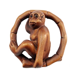 May include: A wooden monkey figurine carved in a sitting position, holding onto a circular bamboo ring. The monkey has a brown finish and black eyes.