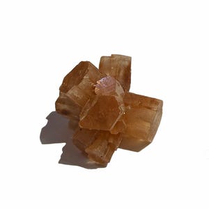 K&ouml;nnte beinhalten: Ein Cluster aus bernsteinfarbenen Aragonitkristallen. Die Kristalle haben eine geometrische, blockartige Struktur und sind radial angeordnet. Das Mineral hat eine durchscheinende Qualit&auml;t, wobei sich das Licht auf den Facetten spiegelt.