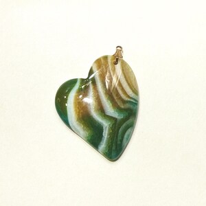 Puede incluir: Colgante en forma de coraz&oacute;n con una fianza dorada. El colgante presenta un patr&oacute;n arremolinado de colores verde, blanco y marr&oacute;n. La piedra tiene un acabado pulido y brillante.