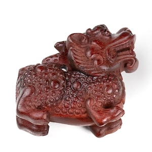 May include: A small, intricately carved wooden figurine of a mythical creature, possibly a dragon or a lion, with a red-brown color and a detailed, textured surface.