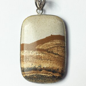 May include: A silver pendant featuring a rectangular, brown, white, and black landscape-patterned stone.
