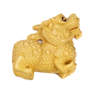 May include: A small, intricately carved wooden figurine of a mythical creature, possibly a dragon or a lion, with a detailed textured surface and a fierce expression. The figurine is a light yellow color.