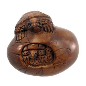 May include: A hand-carved wooden turtle sculpture, with a smaller turtle emerging from a cracked egg. The sculpture is made of dark brown wood and has a smooth, polished finish.