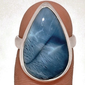 May include: A silver ring featuring a large, teardrop-shaped gemstone. The stone has a swirling, marbled appearance with shades of blue and white. The ring's band is a simple, polished silver.