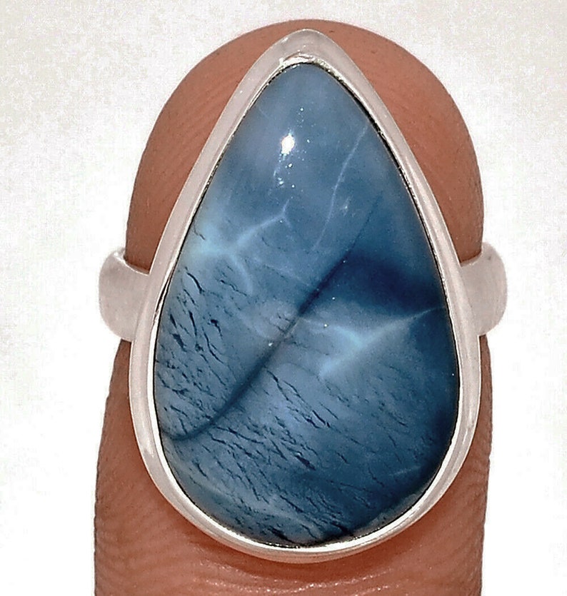 May include: A silver ring featuring a large, teardrop-shaped gemstone. The stone has a swirling, marbled appearance with shades of blue and white. The ring's band is a simple, polished silver.