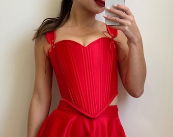 May include: A red corset top with a sweetheart neckline and a matching red skirt. The corset has boning and a busk closure. The skirt is a-line and has a high waist.