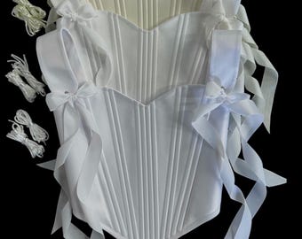 May include: Three white corsets with vertical ribbing and ribbon ties. The corsets have a sweetheart neckline and shoulder straps with bows. The image is set against a black background, highlighting the details of the garments.