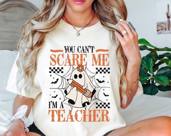 May include: White t-shirt with a ghost holding a pencil and the text "You can't scare me I'm a teacher".