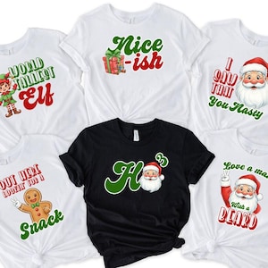 May include: A selection of white and black t-shirts featuring festive Christmas designs. The shirts display images of Santa Claus, elves, and witty slogans such as "Nice-ish" and "Love a man with a beard". The shirts are likely made of cotton.