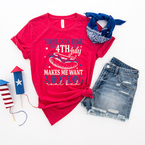May include: A red t-shirt with the text "You look like the 4th of July makes me want a hot dog real bad" is paired with denim shorts and a blue bandana. Two decorative firework models complete the patriotic theme.
