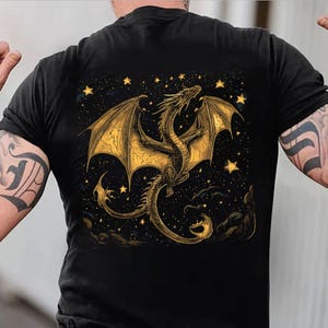 May include: Black t-shirt featuring a golden dragon design with outstretched wings, set against a starry night sky. The dragon is intricately detailed, with a long tail and detailed wings. The design includes stars and clouds.