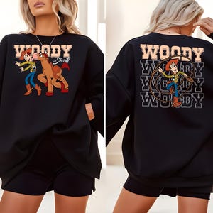 Puede incluir: Sudadera negra con un gr&aacute;fico de dibujos animados de Woody y un caballo. La parte delantera de la sudadera tiene la palabra "WOODY Sheriff" en una fuente marr&oacute;n. La parte trasera de la sudadera tiene la palabra "WOODY" repetida tres veces con un gr&aacute;fico de Woody.