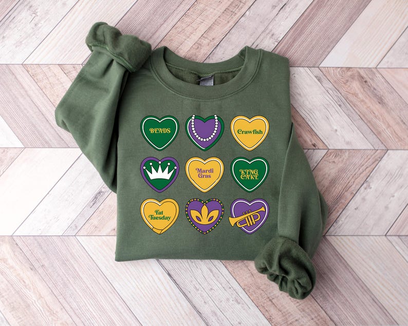 Peut inclure: Sweat-shirt vert sur le th&egrave;me du Mardi Gras. Le sweat-shirt comporte neuf c&oelig;urs avec diff&eacute;rents symboles et textes du Mardi Gras, notamment "beads", "crawfish", "Mardi Gras", "King Cake", "Fat Tuesday" et une couronne.