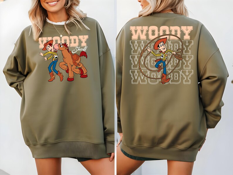 Puede incluir: Sudadera verde oliva con un gr&aacute;fico de dibujos animados de Woody y un caballo en la parte delantera. La parte posterior de la sudadera tiene un gr&aacute;fico de Woody con un lazo y la palabra "WOODY". La sudadera tiene cuello redondo y mangas largas.