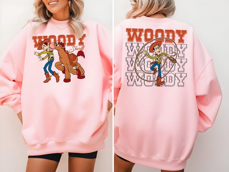 Puede incluir: Sudadera rosa claro con un dise&ntilde;o de dibujos animados de Woody y un caballo. La parte delantera de la sudadera tiene la palabra "Woody" encima del dise&ntilde;o, y la parte trasera tiene la palabra "Woody" repetida varias veces con un dise&ntilde;o de Woody.