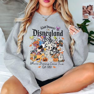 May include: Gray sweatshirt with a graphic of Mickey Mouse and other Disney characters dressed in Halloween costumes. The text "Walt Disney's Disneyland Where Dreams Come True Est. 1955" is printed on the sweatshirt.