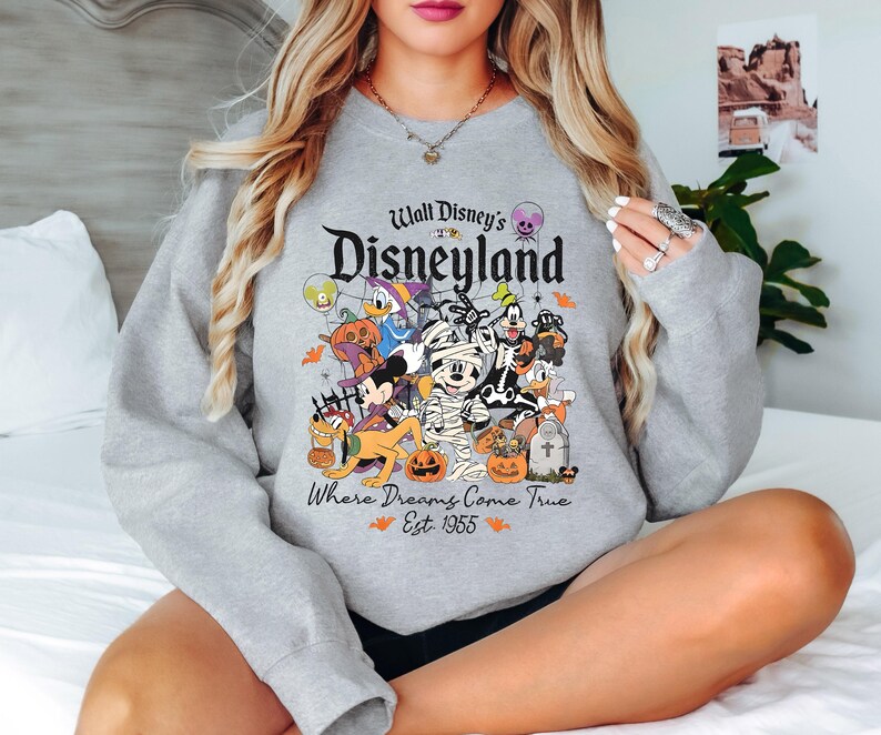 May include: Gray sweatshirt with a graphic of Mickey Mouse and other Disney characters dressed in Halloween costumes. The text "Walt Disney's Disneyland Where Dreams Come True Est. 1955" is printed on the sweatshirt.