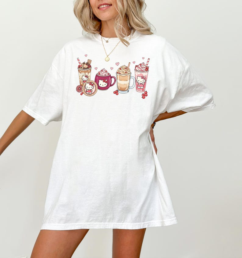 May include: White t-shirt with a graphic of various drinks, such as a milkshake, coffee, and hot chocolate, decorated with cute character designs. The design includes hearts and cherries. The shirt has a relaxed, oversized fit.