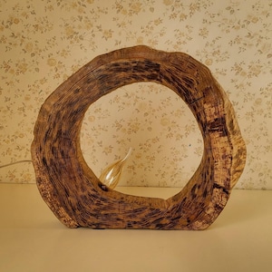 Puede incluir: Una base de lámpara de madera con forma de anillo de árbol con una bombilla en el centro. La base es de color marrón oscuro con veta de madera natural.