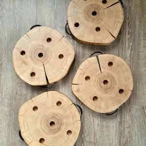 May include: Four natural wood coasters with black metal handles. Each coaster is a circular cross-section of a tree trunk, featuring a central hole and smaller holes around it. The wood has visible grain and cracks.