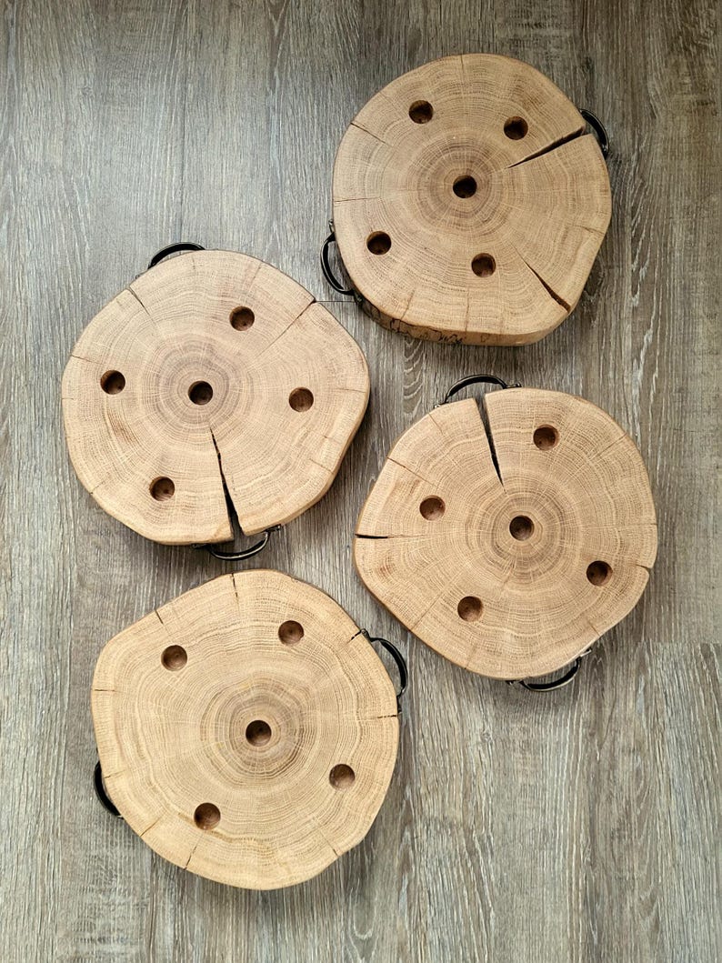 May include: Four natural wood coasters with black metal handles. Each coaster is a circular cross-section of a tree trunk, featuring a central hole and smaller holes around it. The wood has visible grain and cracks.