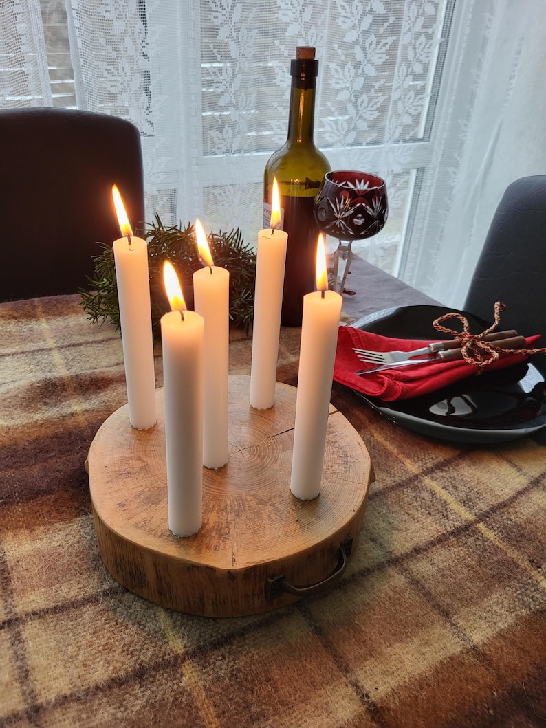 May include: A rustic centerpiece featuring six white candles with lit flames, arranged on a natural wood base. A wine bottle and a decorative glass are also on the table, set on a plaid tablecloth. The scene evokes a warm, inviting atmosphere.