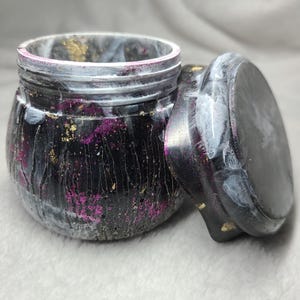 Könnte beinhalten: Eine schwarze und weiße Schmuckschatulle aus Harz mit einem wirbelnden Muster und goldenen Flocken. Der Deckel ist separat und hat ein weißes und schwarzes Marmormuster.