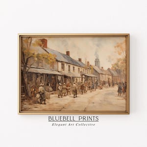 May include: A framed watercolor painting depicts a historical street scene with buildings and figures. The artwork, in warm tones, shows a road lined with shops and people. The text "BLUEBELL PRINTS Elegant Art Collective" is at the bottom.